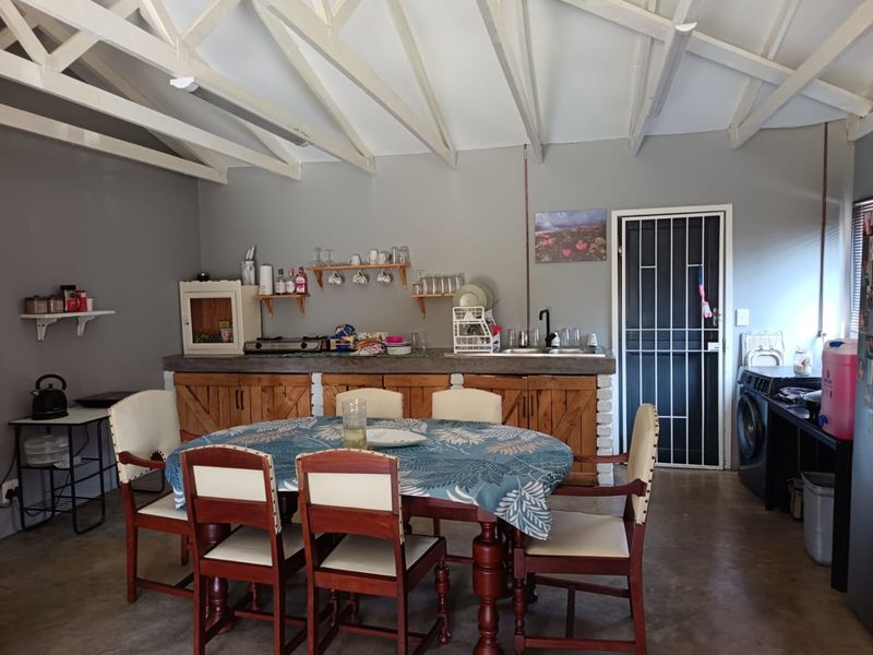 Open-plan kitchen and dining area featuring exposed roof trusses, concrete countertops, and brick-based cabinetry in a rustic, industrial-style space.