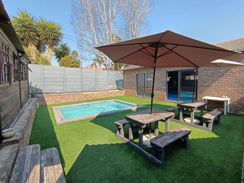 Outdoor entertainment area featuring a swimming pool, artificial lawn, and exposed brick walls, providing a functional space for relaxation and social gatherings.