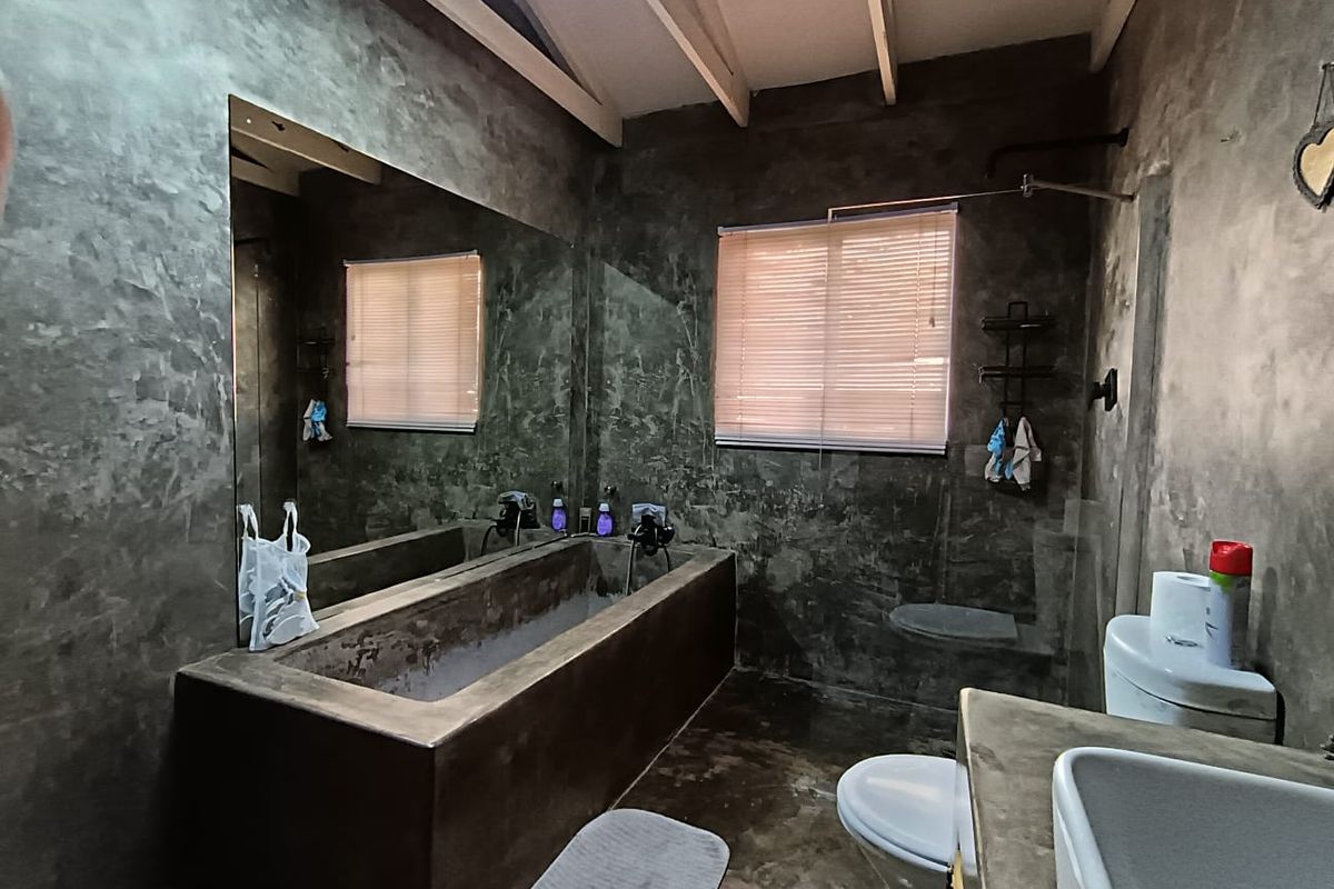 A rustic-style bathroom featuring a custom concrete bathtub, matching concrete vanity with vessel sink, and exposed beam ceiling with a large wall mirror.