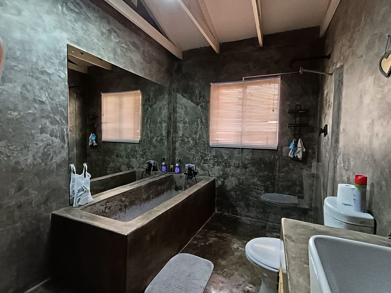 A rustic-style bathroom featuring a custom concrete bathtub, matching concrete vanity with vessel sink, and exposed beam ceiling with a large wall mirror.