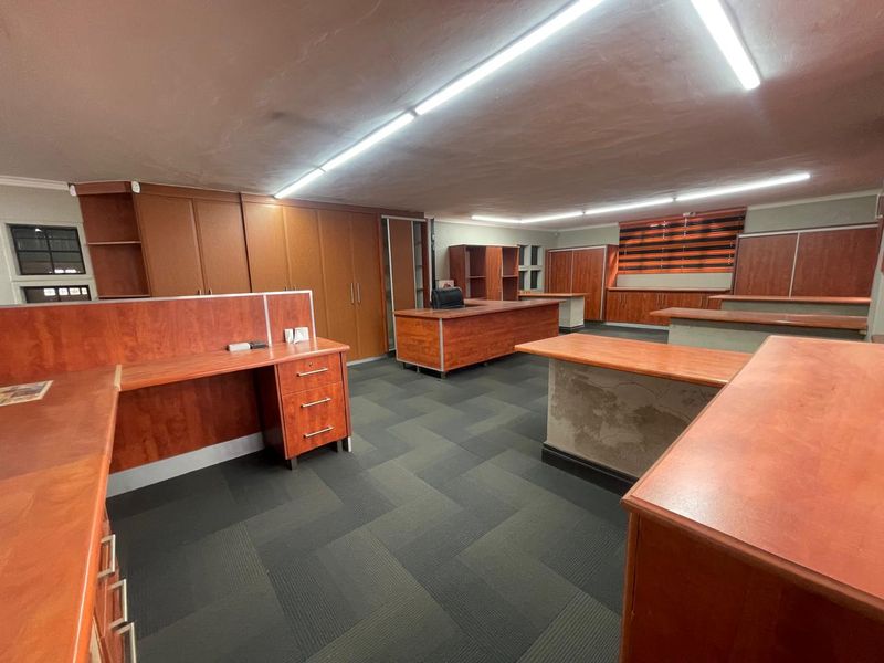 Spacious office area featuring extensive built-in wooden cabinetry, integrated desk workstations, and durable carpet flooring with overhead fluorescent lighting.