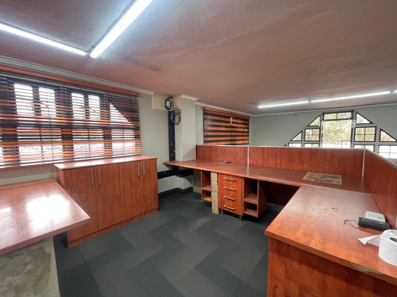 Functional office space featuring built-in wooden cabinetry and desk units, carpeted flooring, and large windows with venetian blinds.