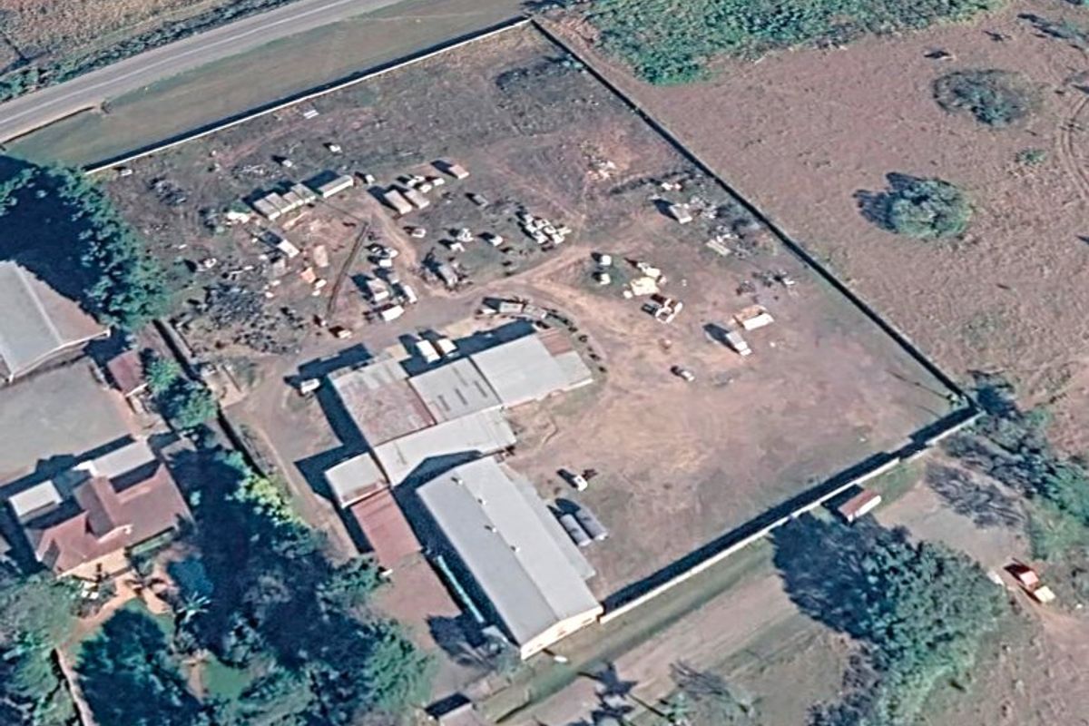 Aerial view of an industrial property featuring multiple metal-roofed warehouse structures and a large, fenced yard area.