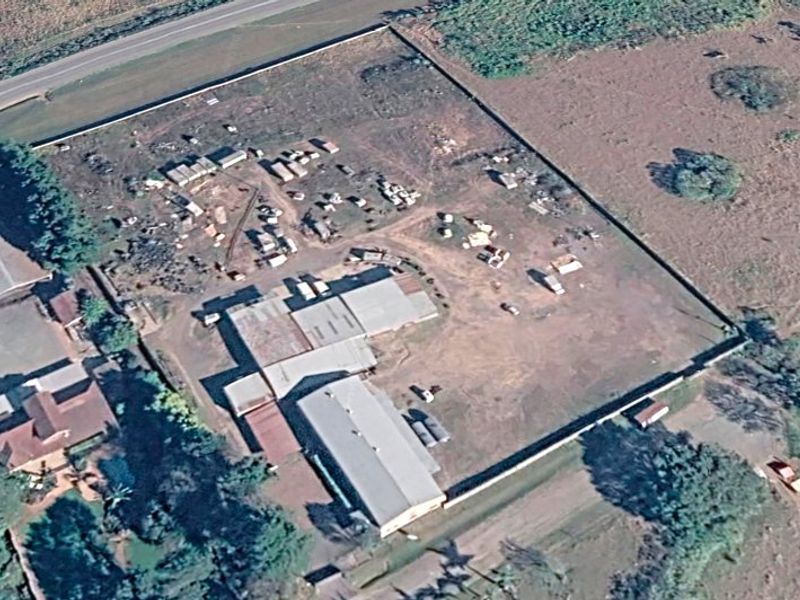 Aerial view of an industrial property featuring multiple metal-roofed warehouse structures and a large, fenced yard area.