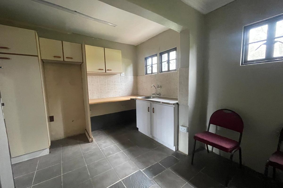 A functional kitchen area featuring built-in cabinetry, a stainless steel sink, tiled backsplash, and tiled flooring, offering a blank canvas for potential renovation.
