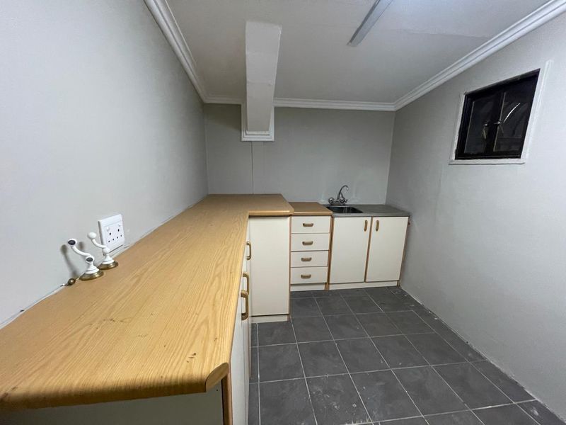 A functional scullery or utility area featuring built-in cabinetry, a laminate countertop, a stainless steel sink, and tiled flooring.