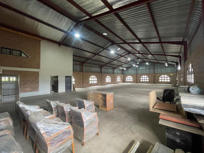 Spacious industrial warehouse or utility space featuring high ceilings with exposed steel trusses, concrete flooring, and natural light through arched windows.