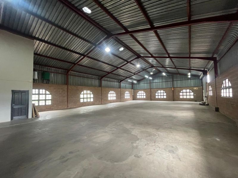 Spacious industrial warehouse or utility space featuring high ceilings with exposed steel trusses, concrete flooring, and arched windows providing natural light.