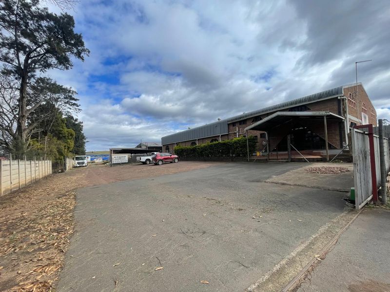 Industrial property featuring a large asphalt driveway, brick facade, and a covered entrance canopy, providing ample space for vehicle access and parking.
