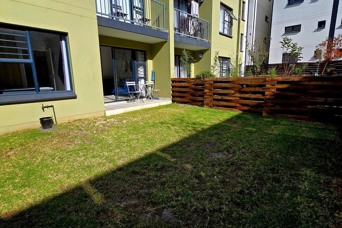 A private rear garden area featuring a small tiled patio, sliding door access to the apartment, and timber perimeter fencing.
