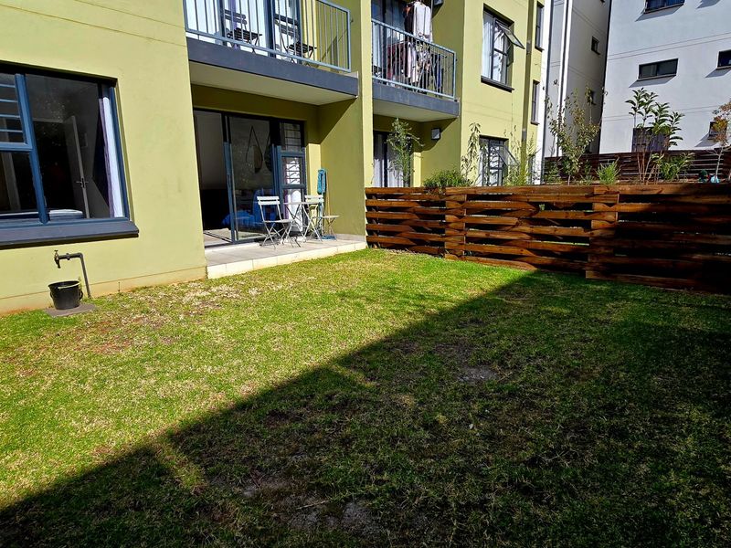 A private rear garden area featuring a small tiled patio, sliding door access to the apartment, and timber perimeter fencing.
