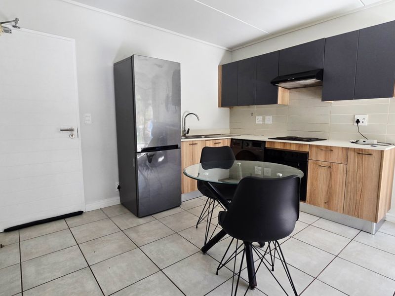 Open-plan kitchen featuring modern two-tone cabinetry, built-in oven and hob, extractor fan, and tiled flooring, seamlessly integrated with the living area.