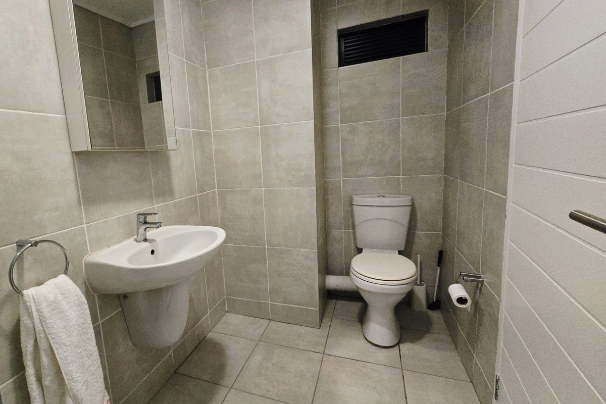 A clean, modern bathroom featuring neutral floor-to-ceiling tiling, a wall-mounted basin, and a standard toilet.