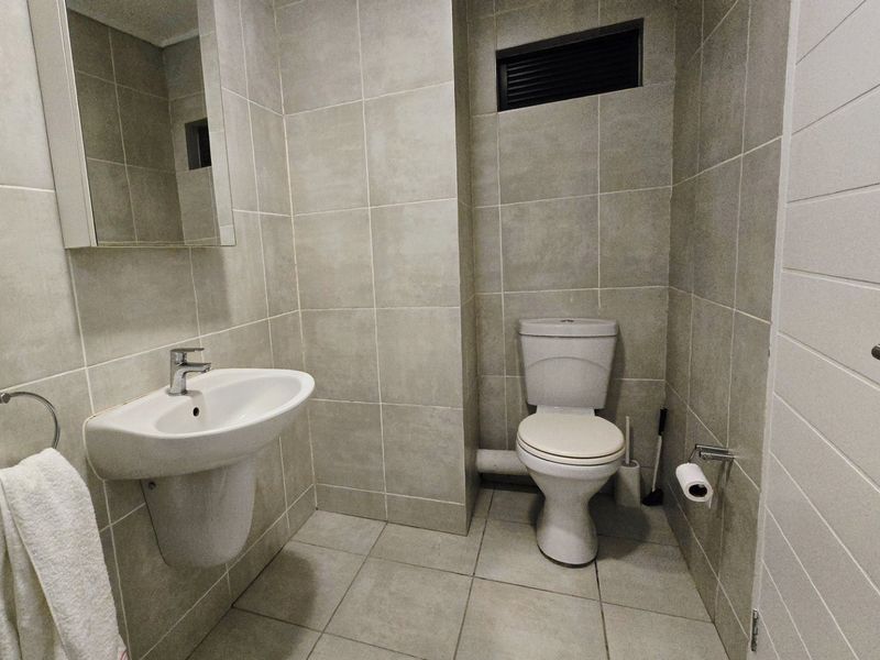 A clean, modern bathroom featuring neutral floor-to-ceiling tiling, a wall-mounted basin, and a standard toilet.