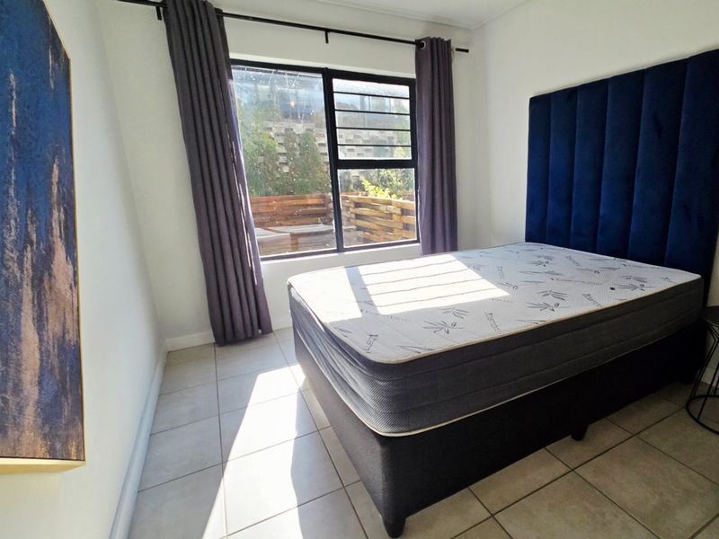 A bright bedroom featuring tiled flooring and a large window with curtain rod, offering natural light and a view of the outdoor area.