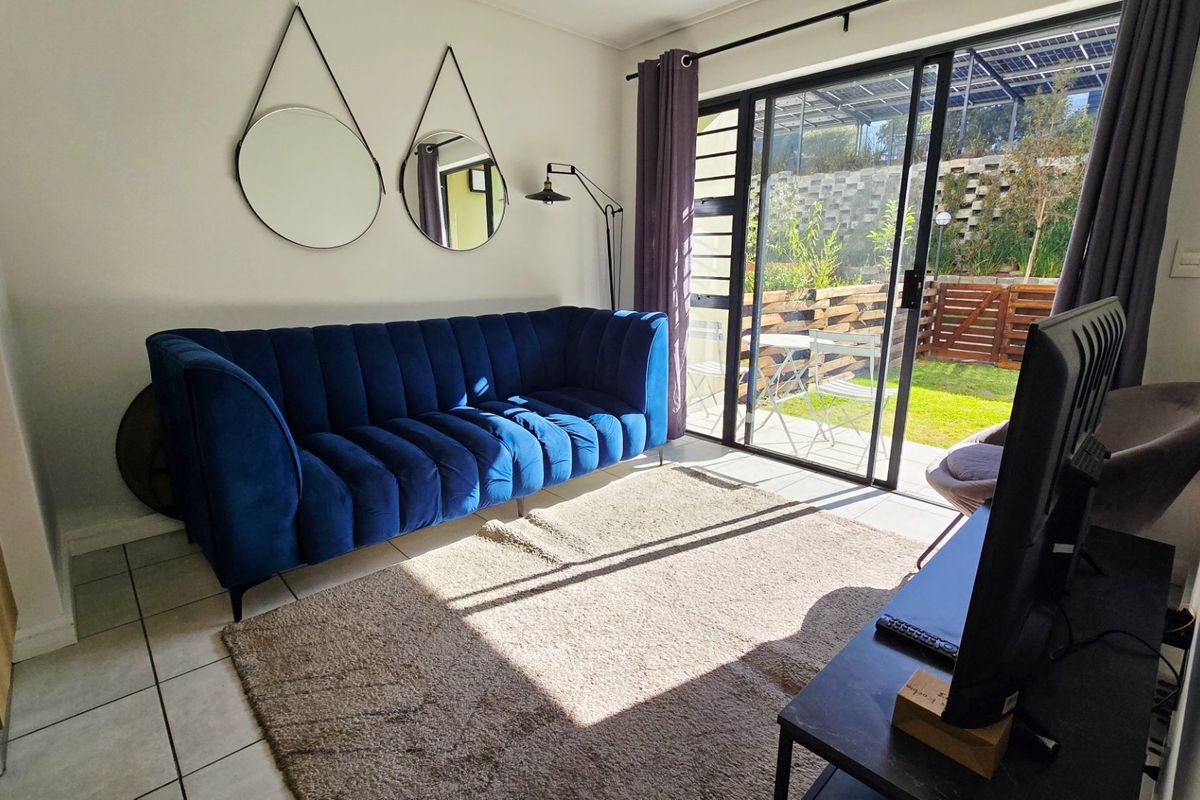 A bright living room featuring tiled flooring and a large sliding glass door providing direct access to the outdoor patio and garden area.