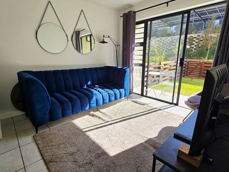 A bright living room featuring tiled flooring and a large sliding glass door providing direct access to the outdoor patio and garden area.
