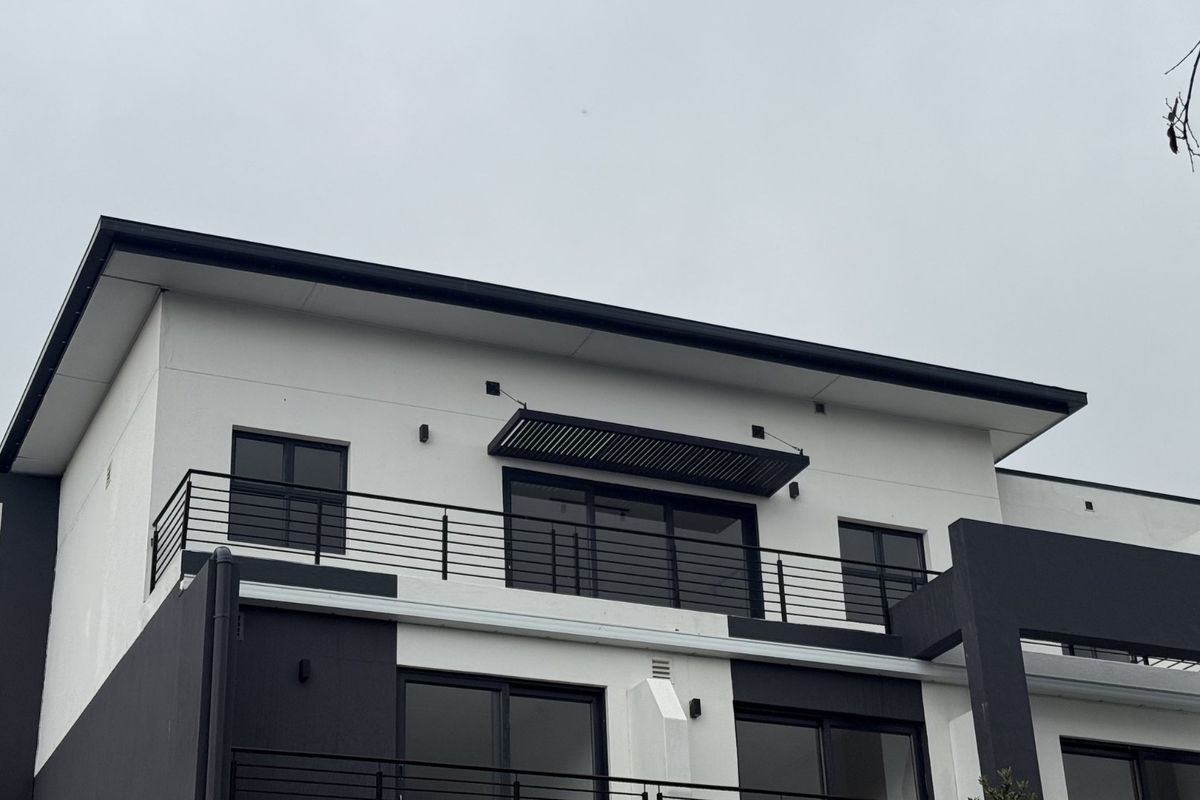 Exterior view of an apartment building featuring a balcony with metal railings, sliding glass doors, and a modern fixed awning.