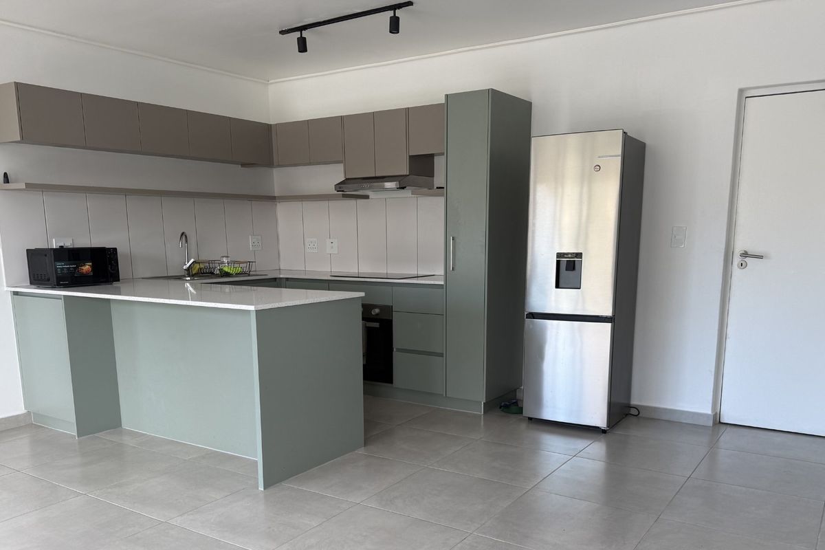 Modern kitchen featuring sage green cabinetry, stone countertops, integrated appliances, and neutral tiled flooring in an open-plan layout.