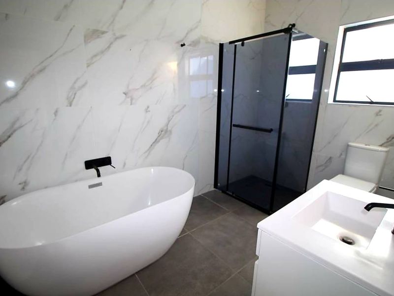 Modern bathroom featuring a freestanding bathtub, walk-in shower with black frame, vanity unit, and elegant marble-look wall tiles.