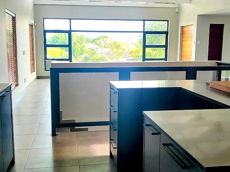 Modern open-plan kitchen and living area featuring sleek dark cabinetry, stone countertops, and expansive windows providing ample natural light and elevated views.