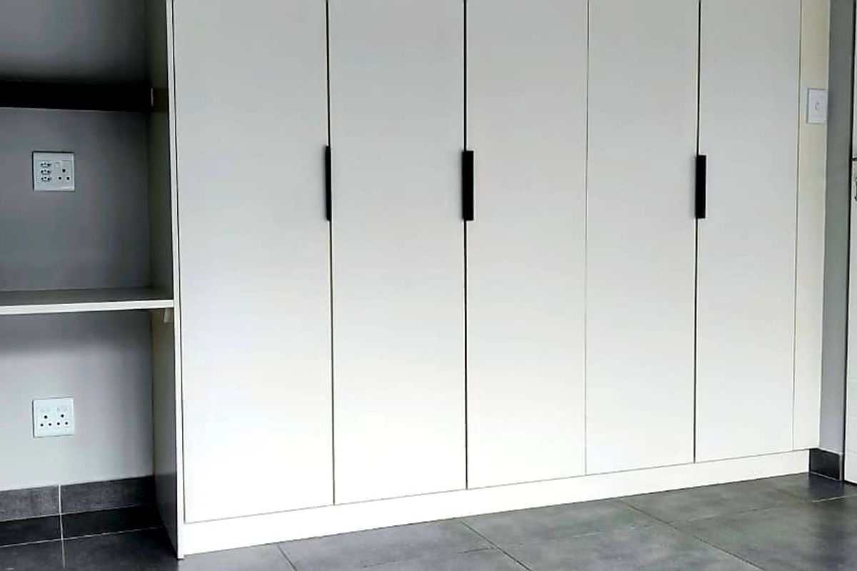 A clean bedroom interior featuring modern built-in cupboards, a built-in desk area, and neutral tiled flooring.