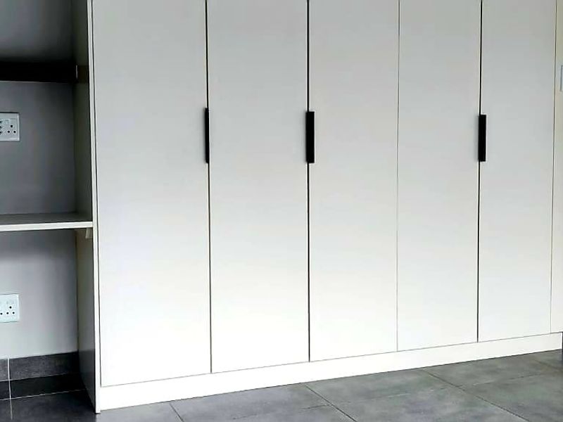 A clean bedroom interior featuring modern built-in cupboards, a built-in desk area, and neutral tiled flooring.