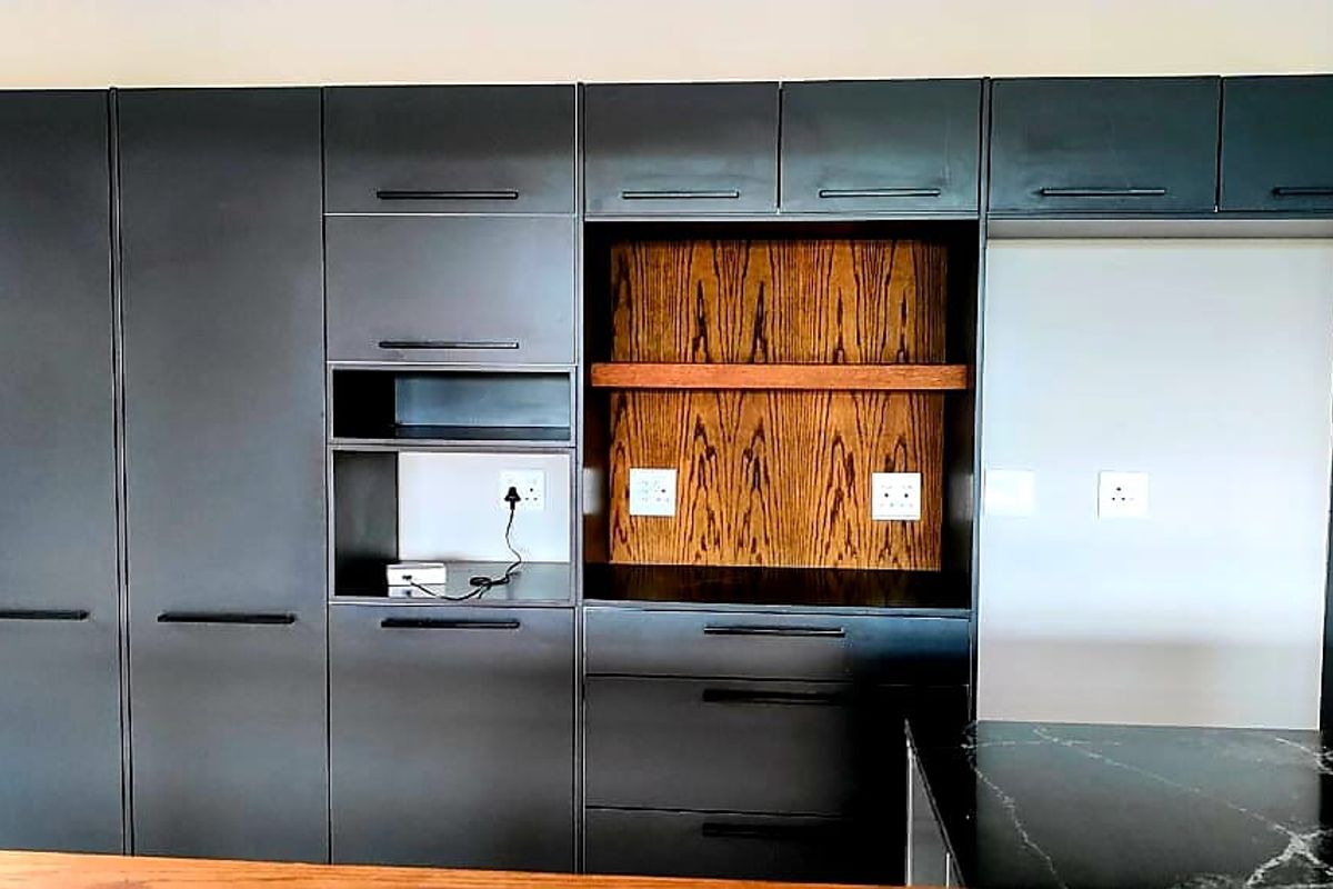 Modern kitchen featuring sleek dark cabinetry, integrated shelving with wood accents, and a dark stone countertop.