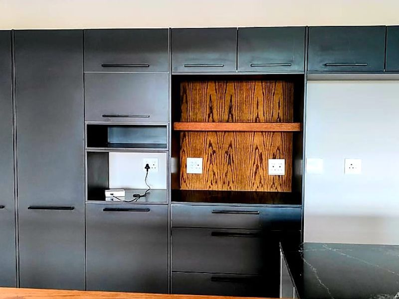 Modern kitchen featuring sleek dark cabinetry, integrated shelving with wood accents, and a dark stone countertop.
