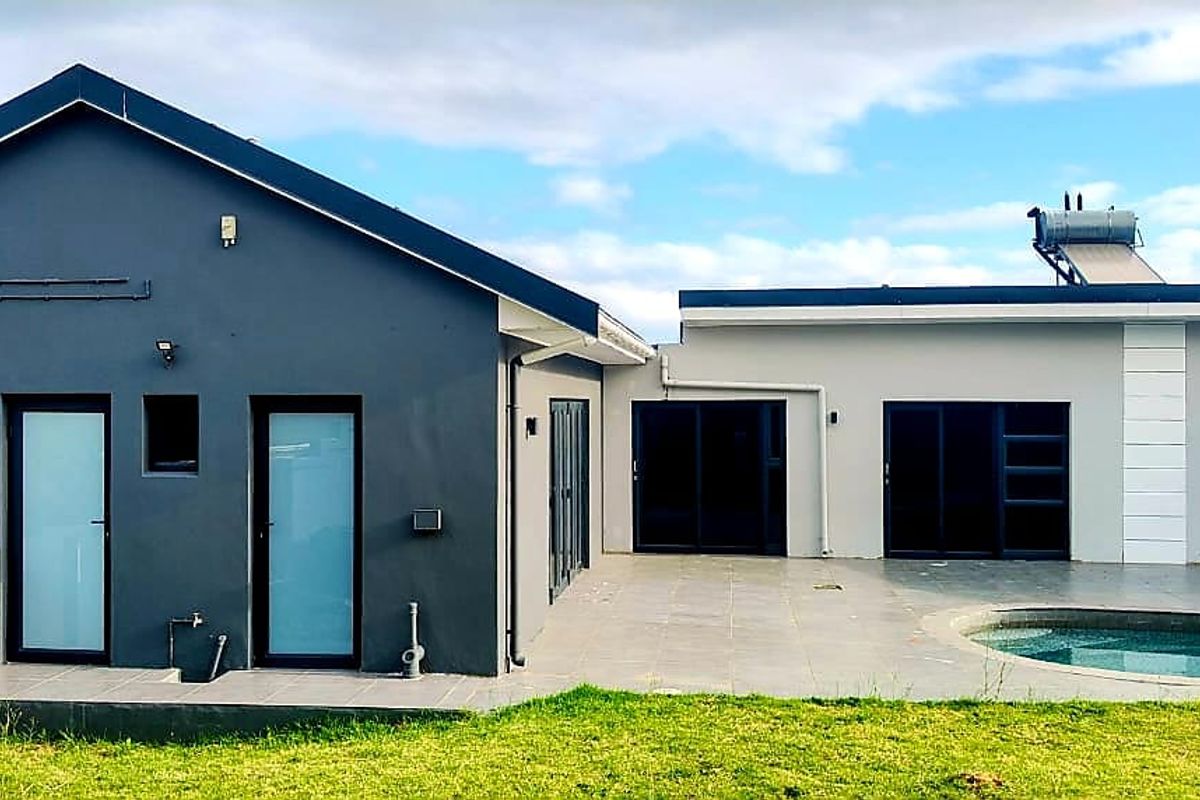 Rear view of the property featuring a tiled patio area, swimming pool, and modern dark-framed sliding doors with a solar water heating system.