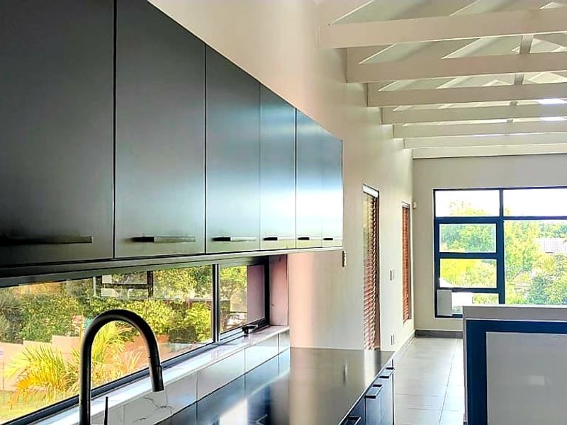 Modern kitchen featuring sleek black cabinetry, stone countertops, and large windows with garden views, complemented by exposed white ceiling beams.