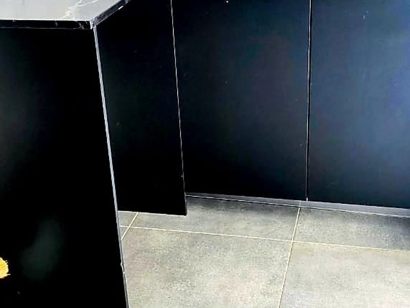 A modern kitchen area featuring sleek black cabinetry, contrasting marble-look wall tiles, a black faucet, and large format floor tiles.