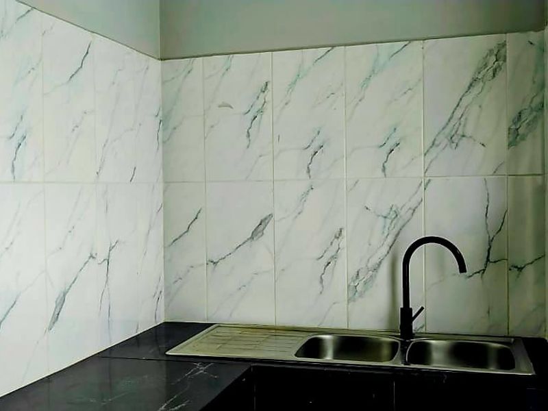 A functional scullery area featuring a double bowl sink with a modern gooseneck faucet, marble-look wall tiling, and a dark countertop.