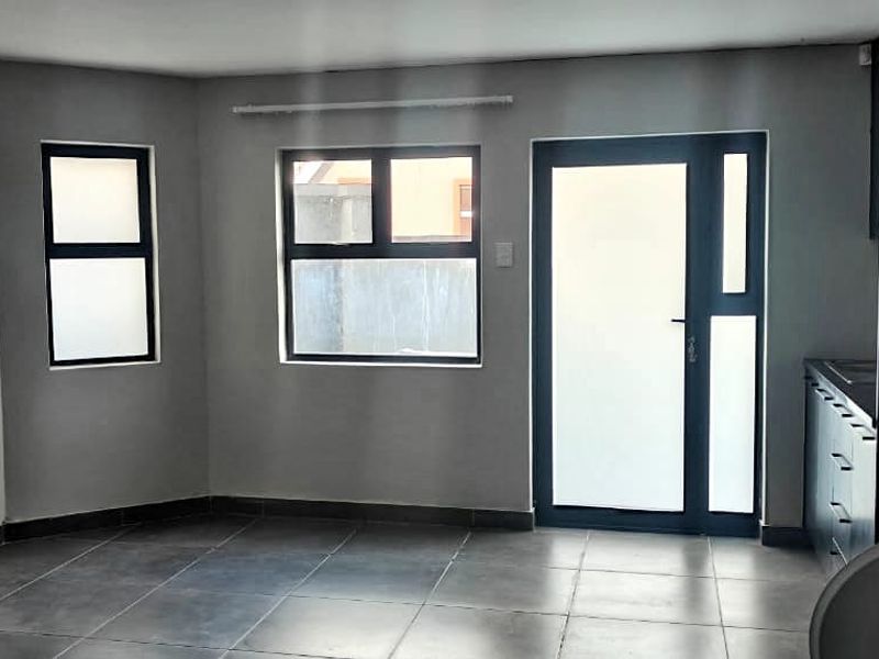 An open-plan living area featuring modern tiled flooring, neutral grey walls, and aluminium-framed windows and door, providing a clean and versatile space.