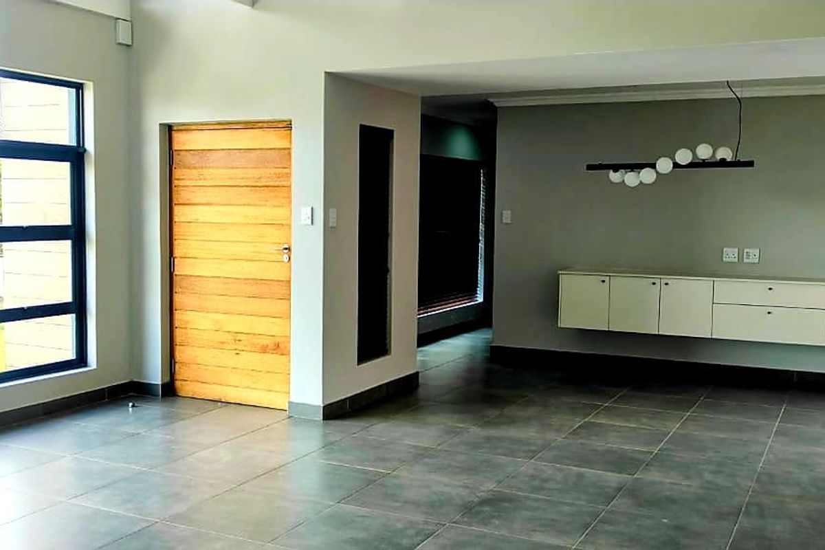 Spacious, light-filled living area featuring large aluminium windows, modern tiled flooring, and sleek wall-mounted cabinetry, offering a clean and contemporary open-plan layout.