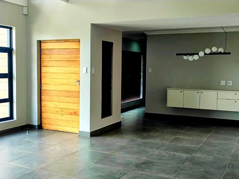 Spacious, light-filled living area featuring large aluminium windows, modern tiled flooring, and sleek wall-mounted cabinetry, offering a clean and contemporary open-plan layout.