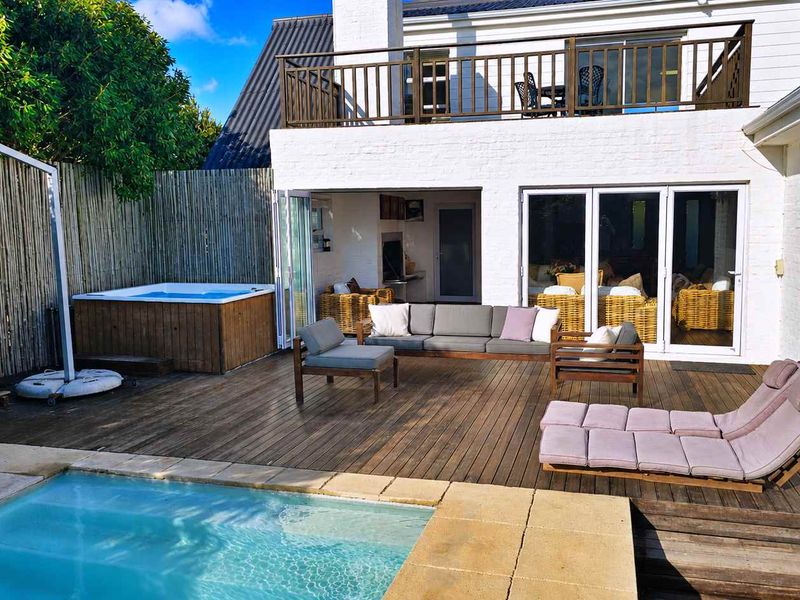 Outdoor entertainment area featuring a swimming pool, timber decking, built-in jacuzzi, and a covered patio with bi-fold doors leading to the main residence.