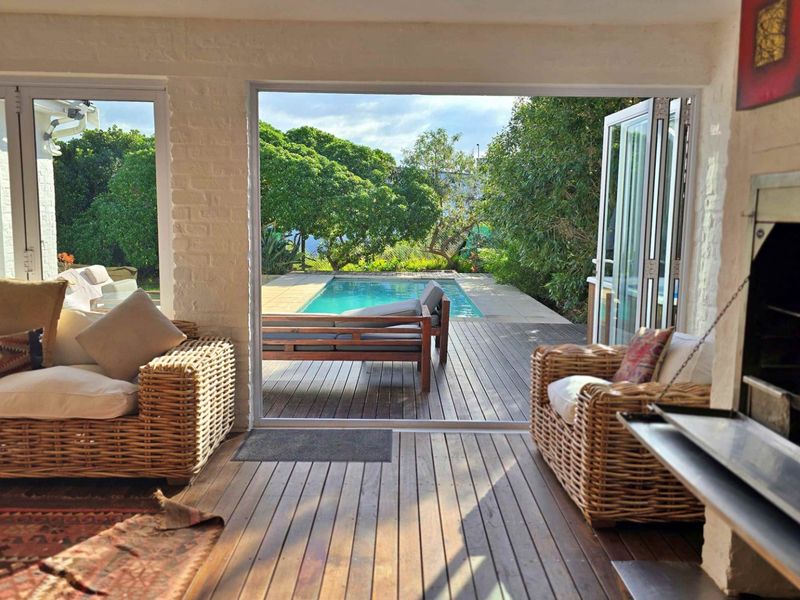 Covered patio area featuring timber decking, a built-in fireplace, and bi-fold doors opening directly onto a swimming pool and garden.