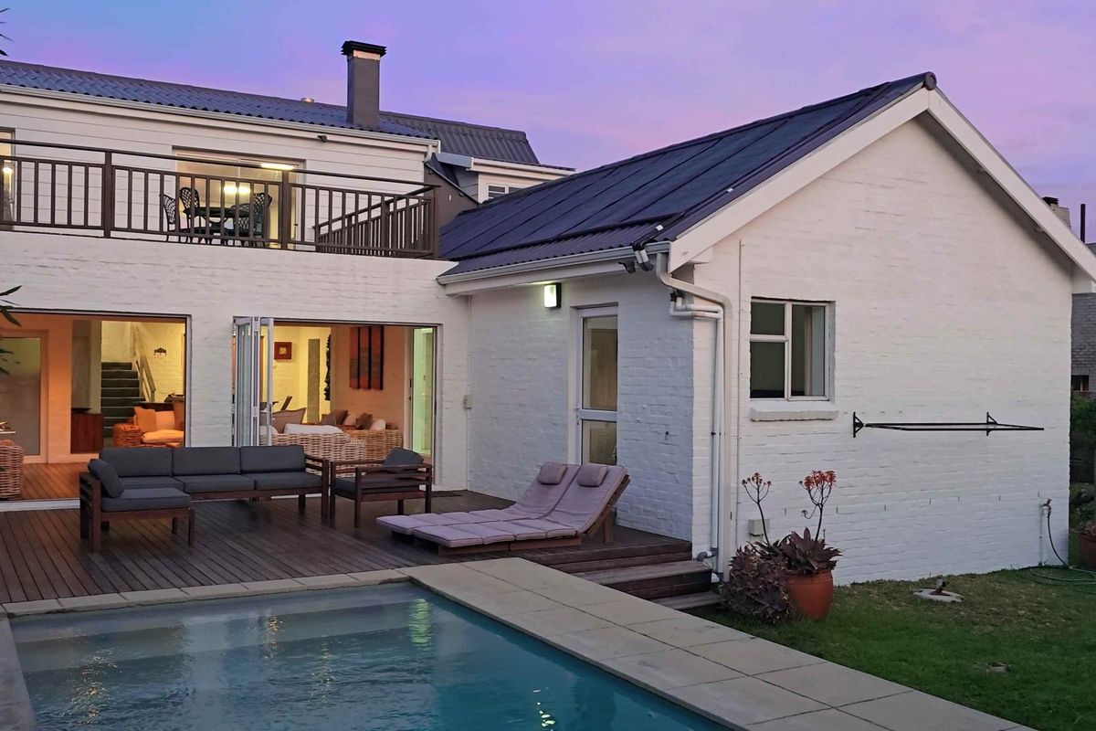 Rear exterior view featuring a swimming pool, timber decking, and a balcony overlooking the garden and house facade.
