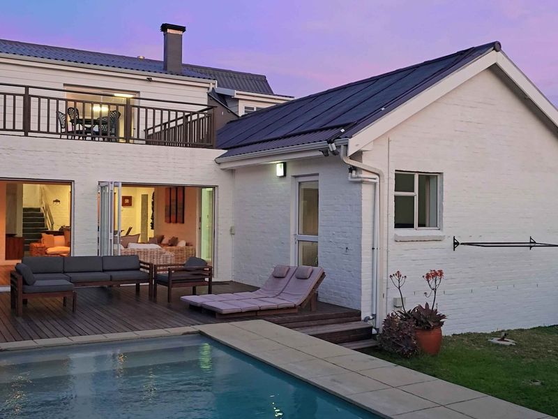Rear exterior view featuring a swimming pool, timber decking, and a balcony overlooking the garden and house facade.