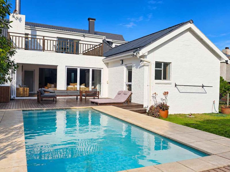 Rear exterior view featuring a swimming pool, timber decking, and a balcony overlooking the garden and white-painted brick facade.