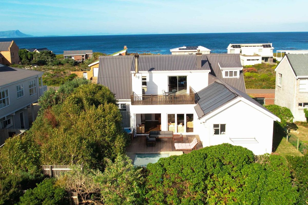 Aerial view of a coastal residence featuring a metal roof, timber decking, swimming pool, and an upper-level balcony overlooking the ocean.