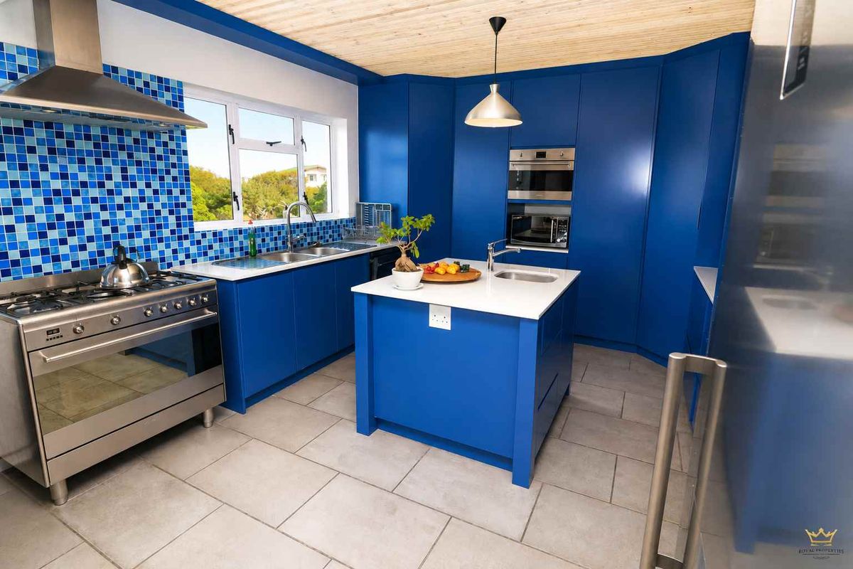 Modern kitchen featuring vibrant blue cabinetry, a central island with a prep sink, stainless steel appliances, and a unique timber-paneled ceiling.