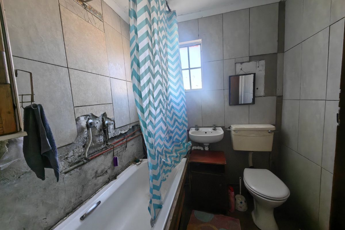 A dated bathroom featuring a bathtub, pedestal basin, and toilet, currently requiring significant repairs to wall tiling and exposed plumbing infrastructure.
