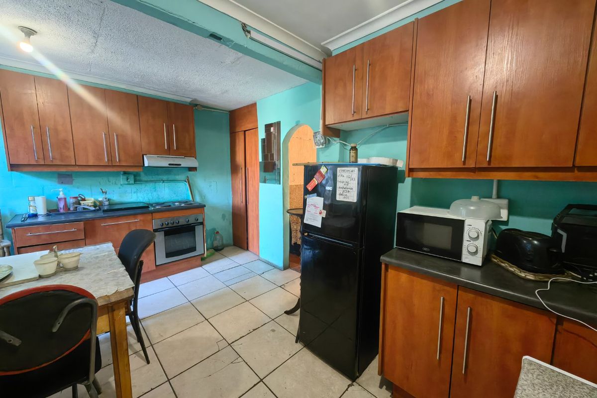 A dated kitchen featuring wood-finish cabinetry, tiled flooring, and an integrated oven and hob, offering significant potential for modernization and renovation.