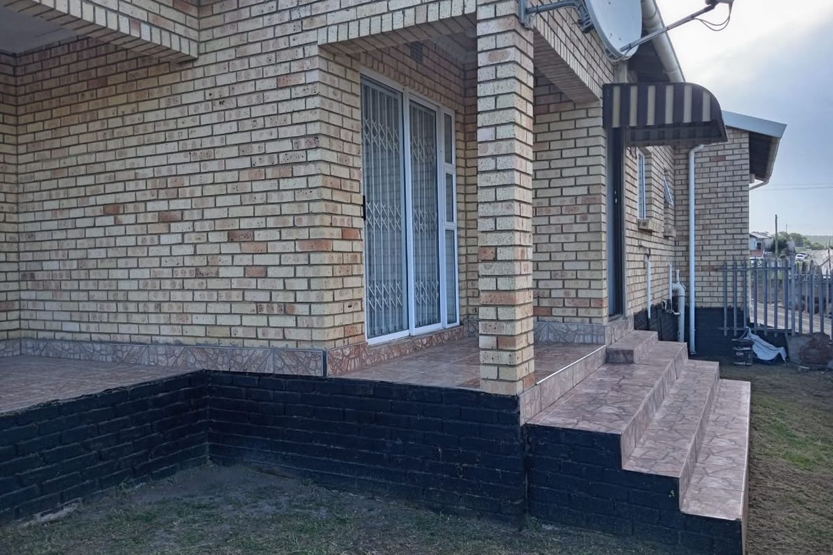 Rear exterior view of a face brick house featuring a tiled patio, security gate, and external steps with a small awning.