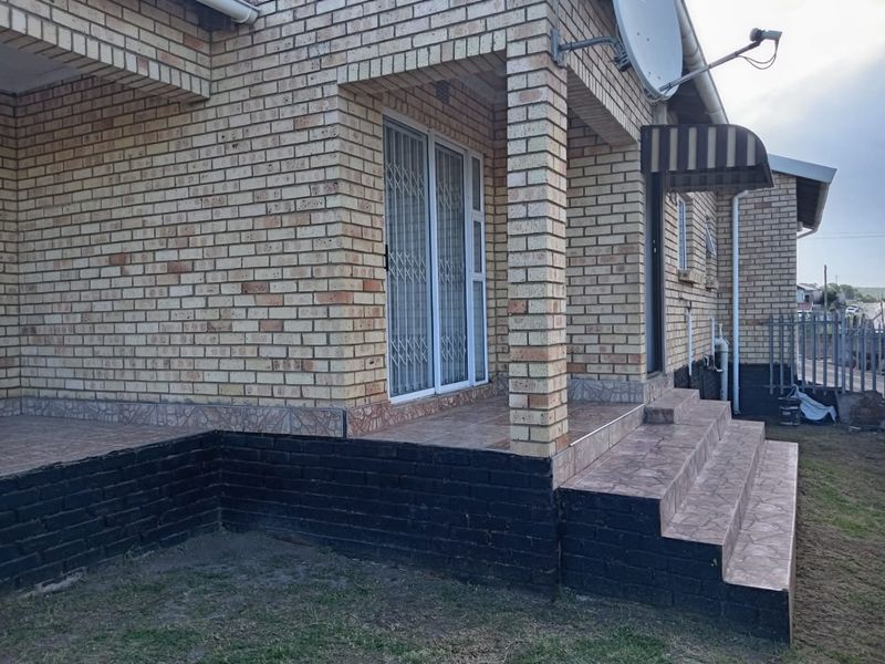 Rear exterior view of a face brick house featuring a tiled patio, security gate, and external steps with a small awning.