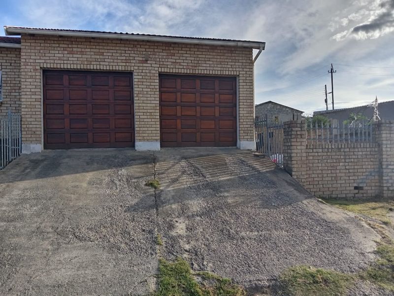 A double garage with wooden doors and a brick facade, featuring a concrete driveway and brick boundary wall with security fencing.