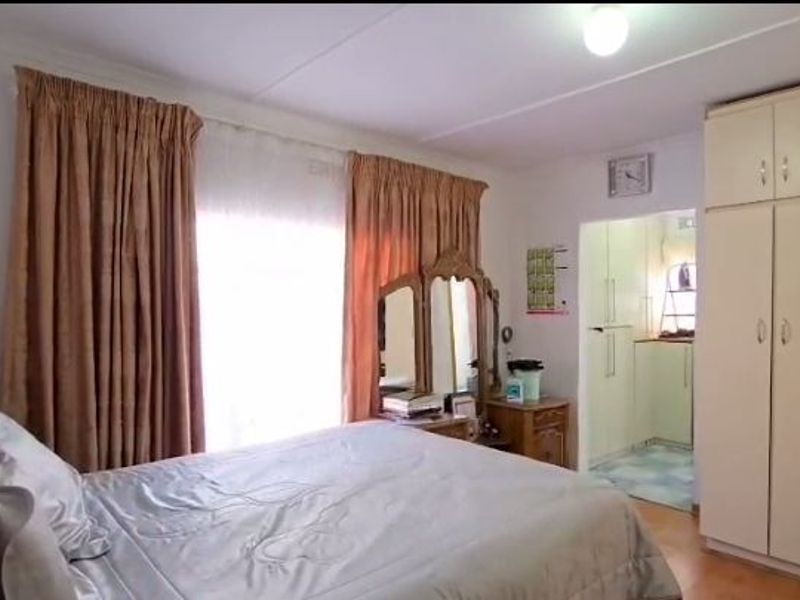 A bedroom featuring built-in cupboards and natural light through large windows, with a view into an adjacent room.