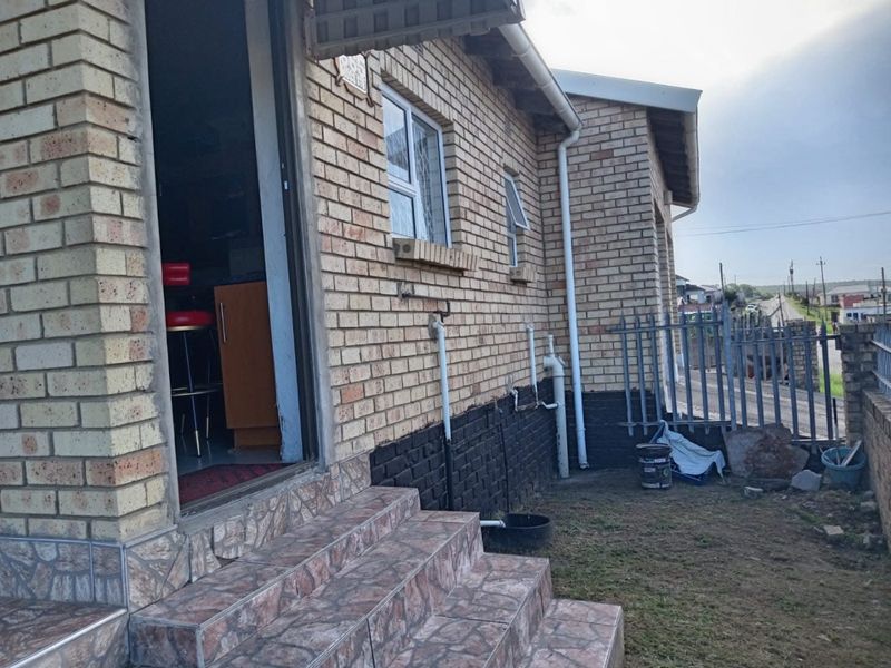 Rear exterior view of a face brick house featuring tiled entrance steps, aluminium windows, and metal security fencing.